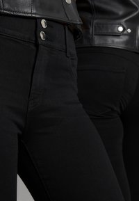 Černé džíny z denimu s hladkou strukturou, vysokým pasem, stříbrnými knoflíky a zadními kapsami.