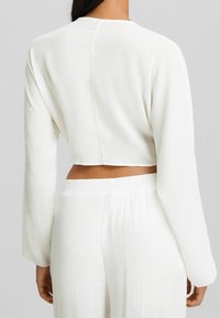 Top corto bianco con maniche lunghe, tessuto texture e cucitura dritta sul retro, abbinato a pantaloni larghi coordinati.