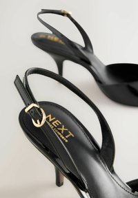 Fekete magassarkú szandálok fényes felülettel, arany csattal ellátott pánttal és elegáns kialakítással. Belsejében jól látható márkajelzés.