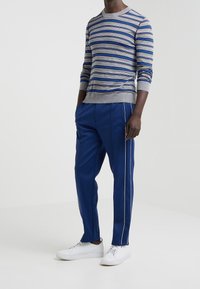 Suéter gris a rayas con líneas azules y rojas, combinado con pantalones azules que tienen piping blanco en los lados y zapatillas blancas.