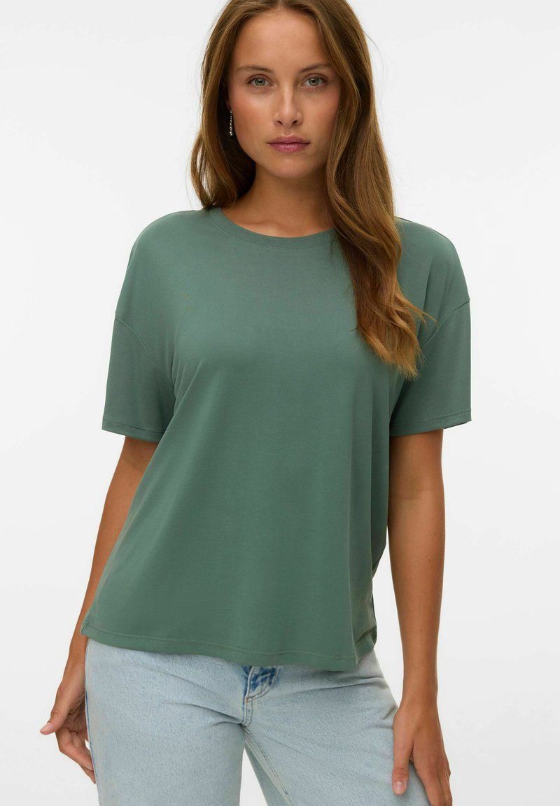 Groene t-shirt met korte mouwen, ronde hals, relaxte pasvorm en een gladde textuur, gecombineerd met lichtblauwe spijkerbroeken.
