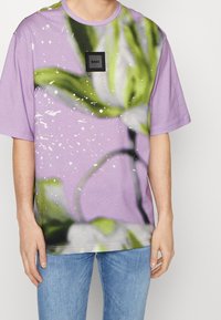 Lavendel färgad bomull t-shirt med ett blommönster och en svart logopatch, med korta ärmar och en avslappnad passform.