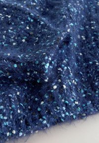 Granatowa tkanina o futrzastej teksturze, z wielokolorowymi plamkami w jasnym niebieskim, białym i ciemniejszych odcieniach, tworząca warstwowy efekt.