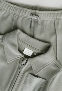 Grå zip-up jakke med krave, tekstureret stof og brystlomme, parret med matchende grå sweatpants med snoretræk.