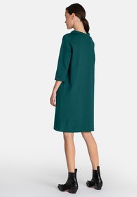 Rochie teal cu un guler strâns și mâneci până la trei sferturi, având o croială dreaptă și accente laterale. Pur și simplu cu botine negre până la glezne.