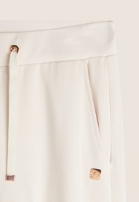 Joggers de un suave tejido en color beige claro, con cordón, dos bolsillos laterales y un pequeño logotipo en tono dorado.