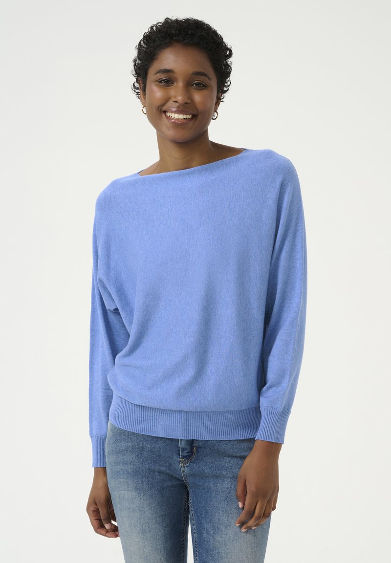 Lichtblauwe oversized trui met een bootnek, geribde manchetten en zoom. Zachte textuur, gedragen met strakke blauwe jeans. Eenvoudig en ontspannen ontwerp.