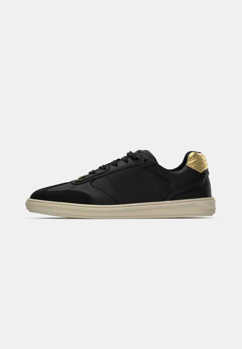Black sneaker with a textured upper, smooth accents, and a gold-highlighted heel. Features a contrasting beige rubber sole and flat laces.