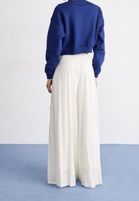 Felpa blu corta abbinata a pantaloni bianchi ampi e plissettati. I pantaloni presentano un tessuto trasparente e testurizzato e una vita elastica.