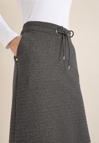 Jupe gris charbon en tissu doux, dotée d'une ceinture élastique avec cordons de serrage et de poches latérales avec des détails discrets en métal.