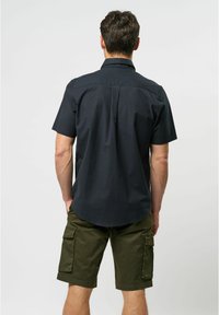 Short-sleeve black shirt with a straight collar, featuring a back pleat and curved hem. Paired with olive green cargo shorts with pockets.
