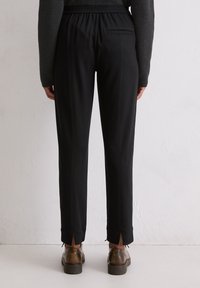 Zwarte cropped broek met een trekkoord in de taille, een achterzak en splitten aan de zoom, gecombineerd met bruine veterschoenen. Glad materiaal.