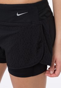 Mustat Nike-shortsit, joissa on teksturoitu design, kaksikerroksinen rakenne ja hopeinen logo vyötäröllä. Venytettävä ja tiukka sisävuori.