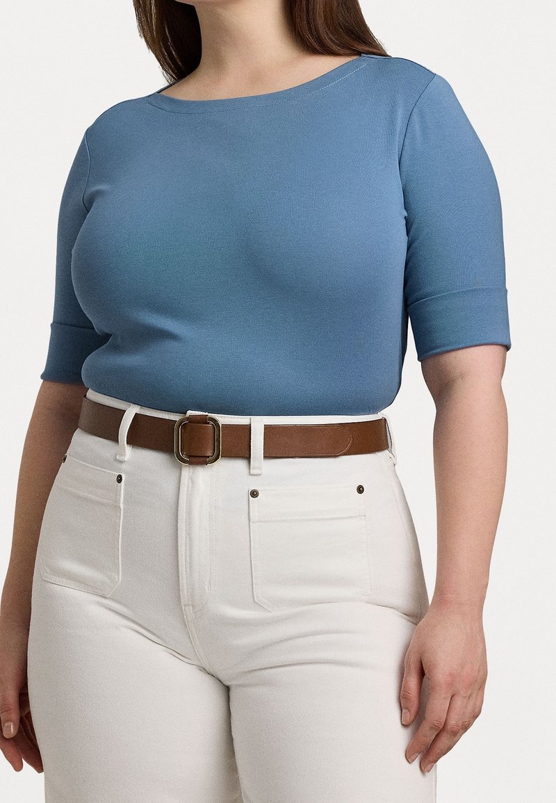 Ljusblått åtsittande topp med trekvartslång ärm, matchat med högmidjade vita jeans och ett brunt bälte med en rektangulär spänne.