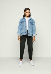 Šviesiai mėlynas džinsinis švarkas su laisvo kirpimo, mygtukų uždarymu ir susuktomis rankovėmis, dėvimas ant balto marškinėlio, derinamas su juodomis kelnėmis ir baltomis sportbačiais.