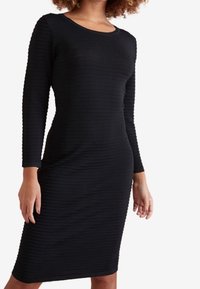 Robe noire à manches longues avec texture côtelée, silhouette ajustée et encolure ronde, s'étendant jusqu'aux genoux.