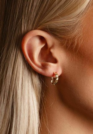 Goldener Creolen-Ohrring, der am Ohr einer Person getragen wird. Der Ohrring weist ein glattes, abgerundetes Design mit polierter Oberfläche auf.