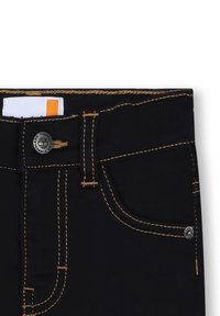 Jeans neri in denim con cuciture gialle a contrasto, dotati di una tasca frontale, chiusura con bottone metallico e un'etichetta con accentuazione arancione.