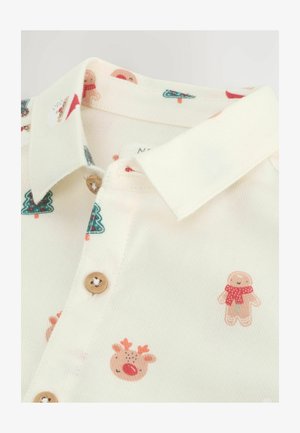 Hvid skjorte med legende trykte mønstre, der viser ingefærmænd, rensdyr og juletree. Træknapper ved kraven.