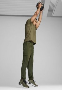 Top deportivo verde oliva y pantalones cargo, con bolsillos y puños elásticos, combinados con zapatillas negras y oliva con un diseño de malla.