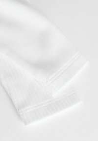 Tissu en coton blanc avec une texture côtelée aux poignets ; présente des lignes épurées et une finition lisse. Les bords sont soigneusement cousus.