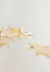 Goldfarbene Ohrringe mit geriffeltem, skulpturalem Design. Sie verfügen über einen zylindrischen Stecker und strukturierte Akzente. Glatte metallische Oberfläche.