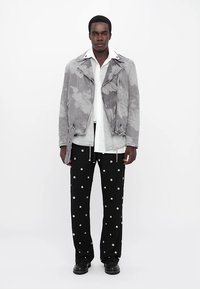 Jachetă de piele gri din denim cu model floral, cămașă albă, pantaloni negri cu buline albe și cizme negre.