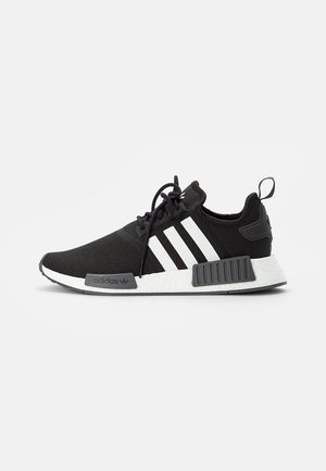 Baskets Adidas NMD noires avec trois bandes blanches, semelle blanche rembourrée, entretoises de semelle intermédiaire noires et lacets noirs, montrées en profil droit.