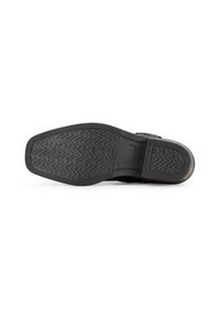 Dessous de chaussure en cuir noir avec une semelle en caoutchouc texturé présentant un motif en zigzag et une zone de talon lisse. Détail de boucle visible sur le côté.