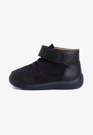 Dětská černá semišová bota s koženým páskem, kulatou špičkou, perforovanými detaily a strukturovanou gumovou podrážkou pro přilnavost a flexibilitu.