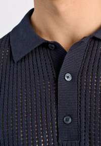 Granatowy sweter polo z dzianiny z teksturowanym wzorem, zapięcie na guziki z dwoma ciemnymi guzikami oraz klasycznym kołnierzykiem.