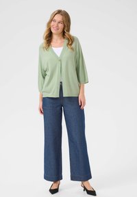 Un cardigan vert clair à manches courtes, avec une fermeture à un seul bouton et une coupe décontractée, associé à un pantalon en denim bleu à jambes larges.