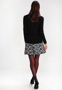 Suéter negro de canalé combinado con una falda acampanada con un patrón geométrico en blanco y negro. La modelo lleva pantyhose negras transparentes y tacones.