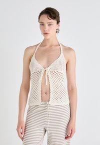 Heklet topp med halterneck i kremfarge, med åpen arbeidsdesign, knyting foran, bølgede kanter og en løs passform kombinert med stripete bukser.