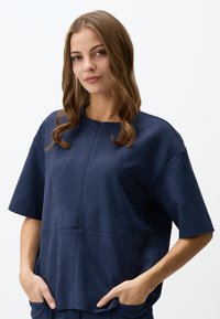 Top blu navy a maniche corte realizzato in tessuto morbido, con scollatura rotonda e due tasche laterali. Texture liscia con cuciture visibili.