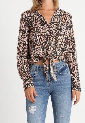 Žena nosící dlouhý rukáv, halenku s leopardím potiskem uvázanou v pase, ve spojení se světle modrými roztrhanými džínami.