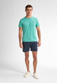 Světle modré tričko s krátkým rukávem v kombinaci s námořnickými šortkami s malým geometrickým vzorem. Bílé tenisky dotvářejí celkový vzhled.