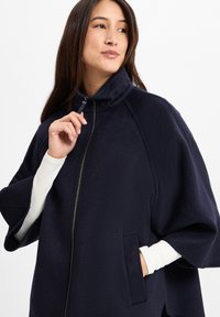 Granatowy polarowy płaszcz z wysokim kołnierzem, z przodu na zamek błyskawiczny oraz z bocznymi kieszeniami; ma luźny krój i miękką teksturę.