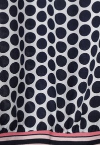 Vit tyg med stora oregelbundna svarta prickar och en randig nederkant i rosa, svart och vitt.