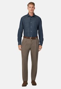 Completo da uomo con una camicia blu scuro con bottoni e pantaloni marrone a righe, completato da una cintura marrone e scarpe in suede.