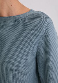 Jasnoniebieski sweter z dzianiny z teksturowanym wzorem, okrągłym dekoltem i luźnym krojem, prezentujący detale z prążkowanej tkaniny.