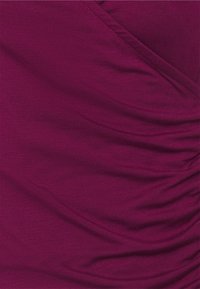 Top ajustado en un tejido morado profundo con una textura suave, que presenta detalles fruncidos y un diseño cruzado en la parte delantera.