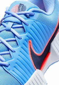 Niebieski sneaker Nike z jasnoniebieskimi sznurówkami, teksturowanym skórzanym panelem, czarno-pomarańczowym logo Swoosh oraz białą podeszwą z pomarańczowym akcentem.