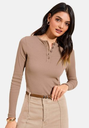 Langärmeliges Henley-Oberteil aus leicht braun geripptem Stoff mit Knopfleiste und rundem Ausschnitt, kombiniert mit einem beigen Rock.