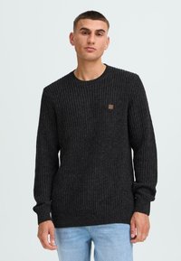 Pulover negru tricotat, cu un guler tip crew și o textură ribbed. Accentuat de o mică patch cu logo maro pe piept. Mâneci lungi.