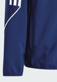 Marineblaue Sportjacke mit glatter Textur, die über weiße Akzentstreifen, eine mit Reißverschluss gesicherte Tasche und elastische Bündchen verfügt.