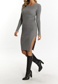 Graues, geripptes Langarmkleid mit seitlichem Schlitz, verziert mit kleinen silbernen Nieten, kombiniert mit kniehohen schwarzen Stiefeln mit Absatz.