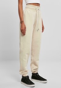 Beige Sweatpants mit einem Kordelzugbund, mit Bündchen an den Knöcheln und Seitentaschen, kombiniert mit schwarzen High-Top-Sneakern. Weiches, strukturiertes Material.