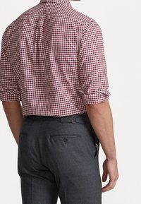 Camicia a quadri rossi e bianchi con maniche arrotolate, abbinata a pantaloni grigi sartoriali con tasche posteriori e dettaglio della cintura.