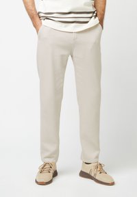 Pantaloni beige intrecciati con una vestibilità dritta, dotati di tasche e una texture liscia, abbinati a sneaker lavorate a maglia beige chiaro.